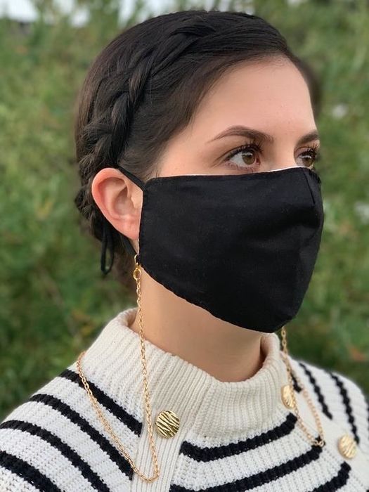 A model is seen wearing a black face mask with a delicate gold face mask chain