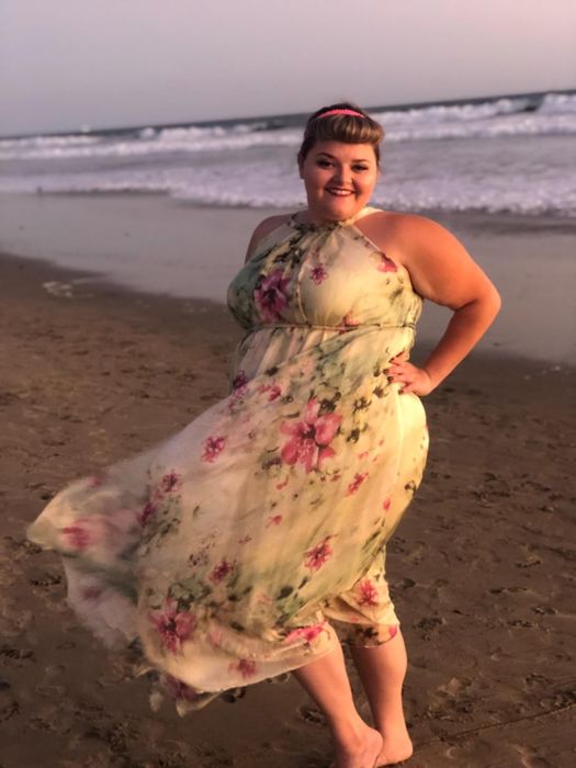 reviewer smiling and posing on a beach, wearing a cream and light green floral halter dress