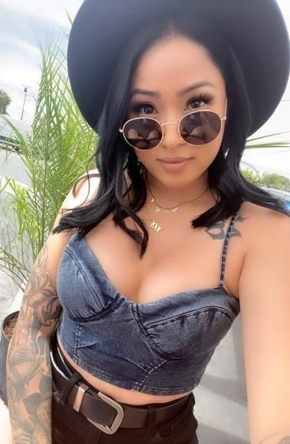 Reviewer is seen wearing black round sunglasses with a black fedora, a denim crop top, and belted black shorts