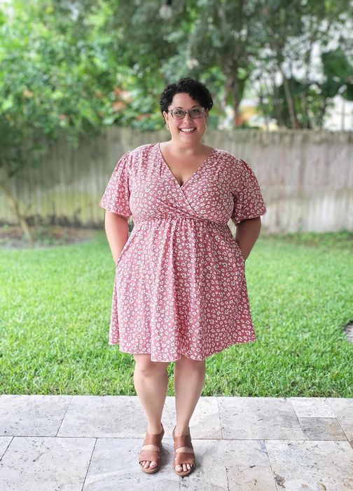 Reviewer standing outdoors with a smile, wearing a floral-patterned short-sleeve dress and sandals