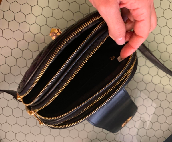 A reviewer demonstrates the three gold-zippered compartments, secured by a turn-lock closure strap