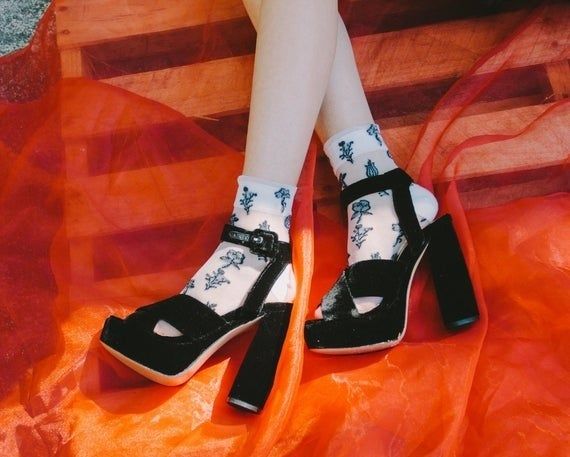 A model is seen wearing white sheer socks with a floral pattern under velvet open-toe platform shoes