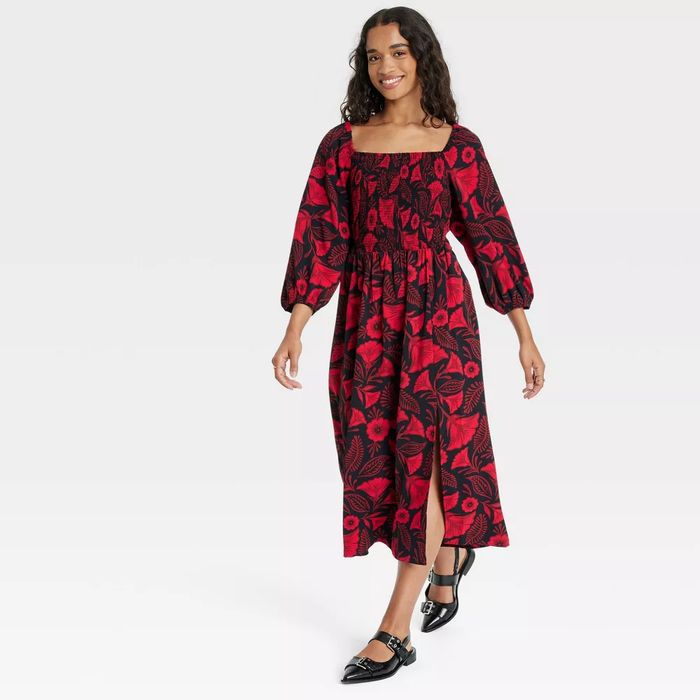 A model wearing a floral dress with puffed sleeves and black flats, confidently walking while smiling.