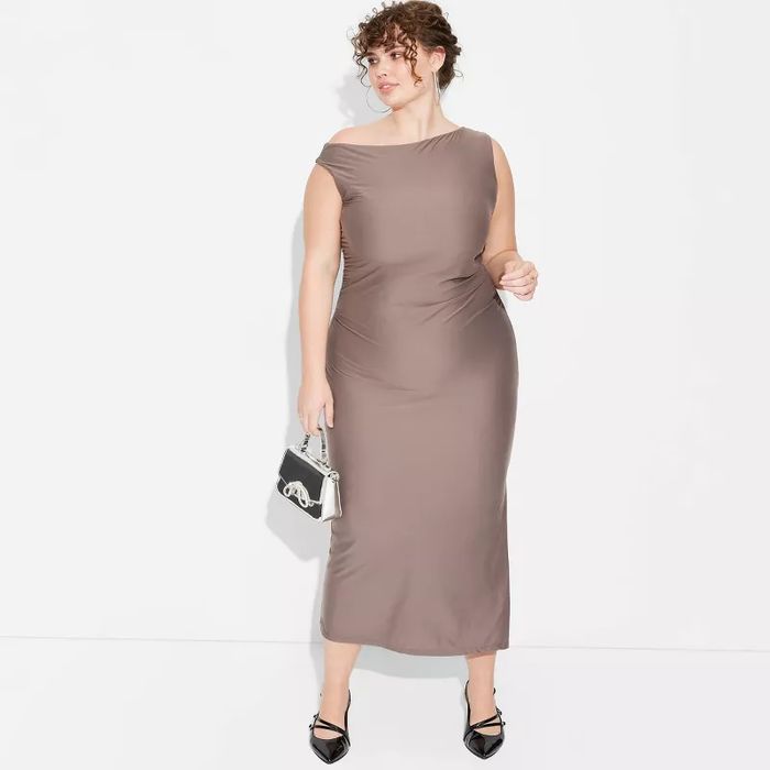 A person is dressed in a sleek, form-fitting off-shoulder dress, holding a small purse and wearing fashionable shoes.