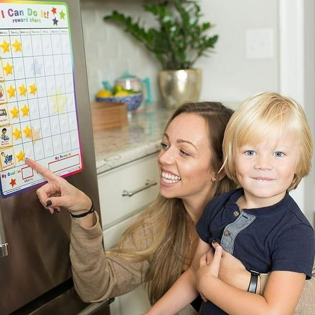 A mom holding her child while pointing at a reward chart