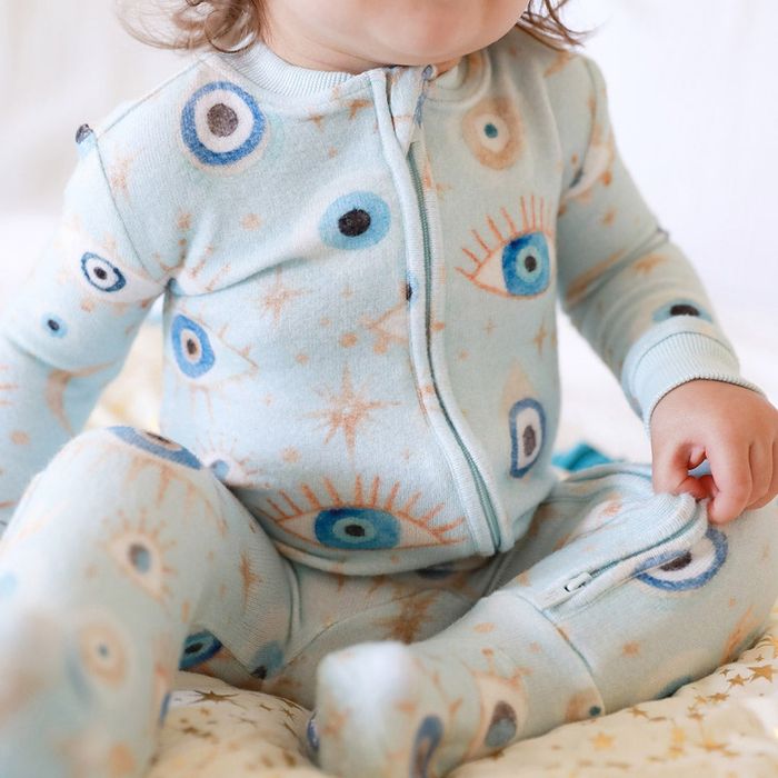 A baby wearing a plush sleeper pajama with an evil eye and celestial print