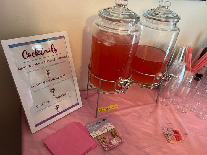 A cocktail menu displayed next to two large drink dispensers on a table, set up for a festive event