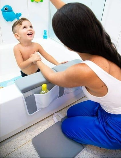 A mom kneeling on a mat, bathing her baby