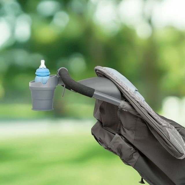 A stroller with an attached cup holder carrying a blue bottle, parked outside.