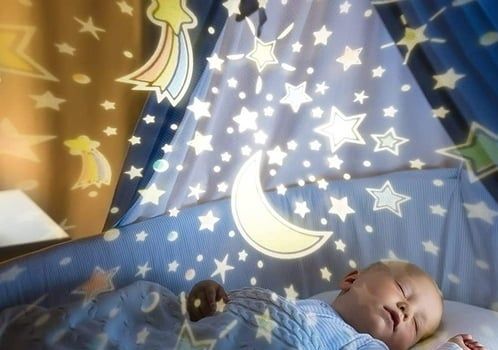 A baby resting in their crib with a galaxy projection on the ceiling