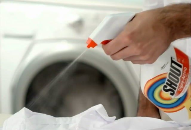 A hand applying stain remover to a white shirt