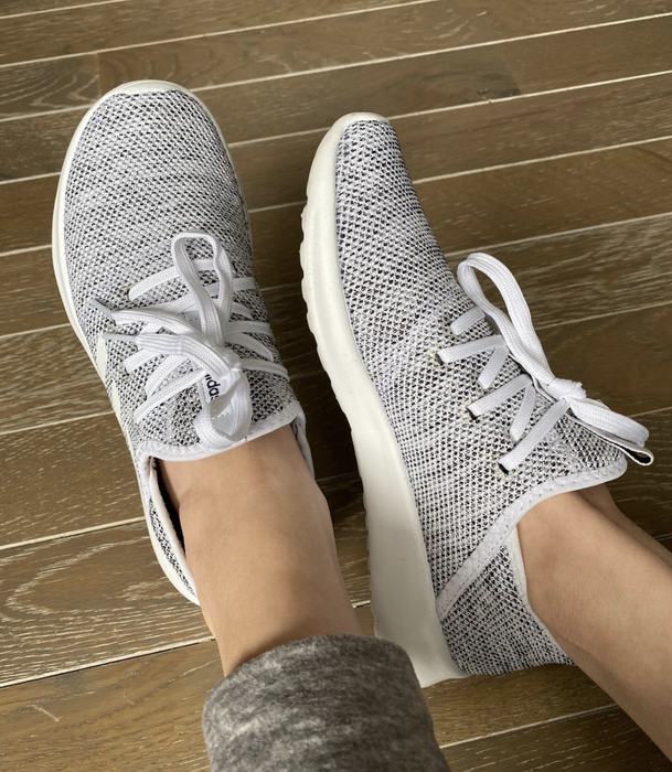 A reviewer wearing gray and white sneakers with white laces