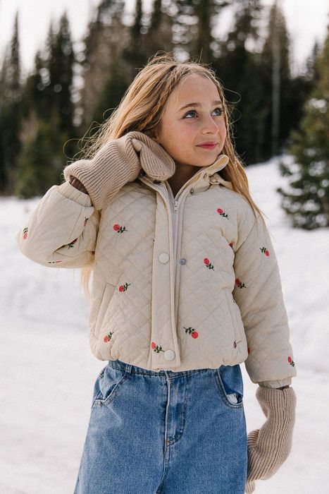 A child in a cream-colored quilted coat adorned with floral patterns