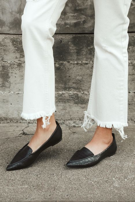 Feet wearing black pointed loafers made of vegan suede
