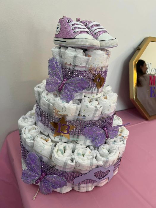 A diaper cake with purple accents and butterflies, topped with baby shoes for a baby shower