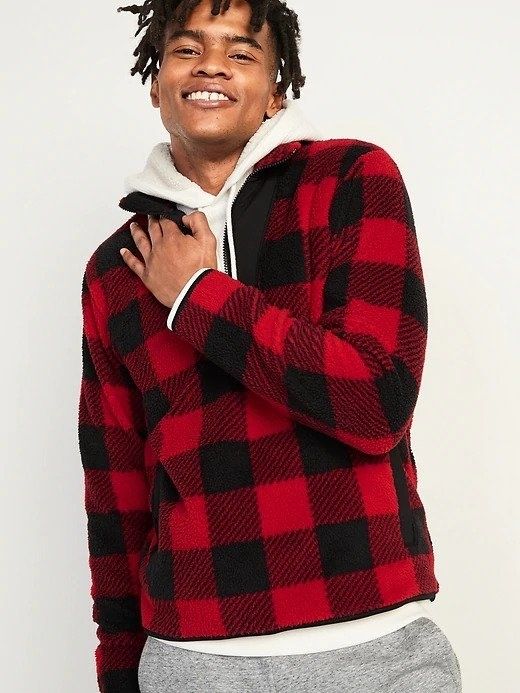 A man wearing a red and black plaid half-zip sweatshirt with a white hoodie peeking out underneath.