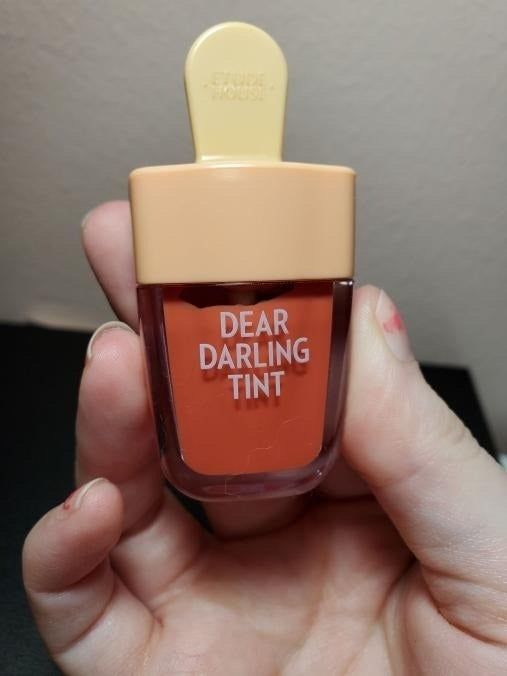 Reviewer holding a popsicle-shaped red lip tint