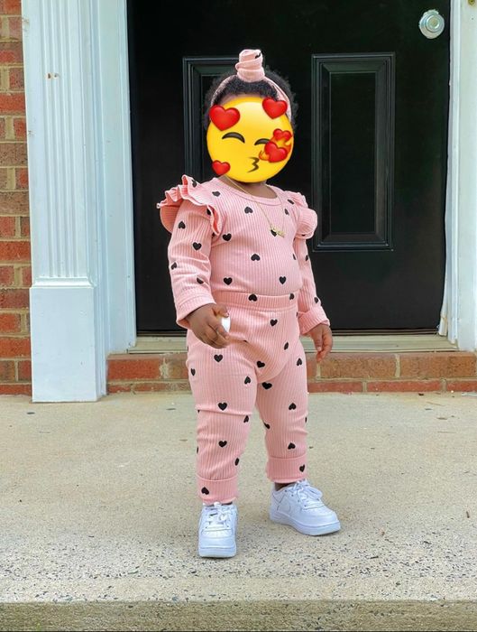 A toddler wearing a pink knit set with black heart designs