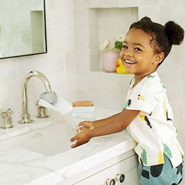 A child happily washing their hands in a sink with water that flows closer to them, thanks to the faucet extenders