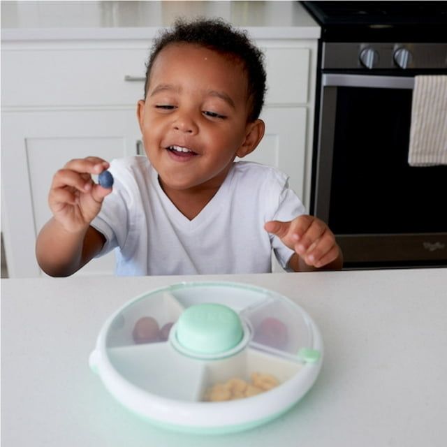 A child smiling at a snack tray with several compartments placed on a kitchen counter