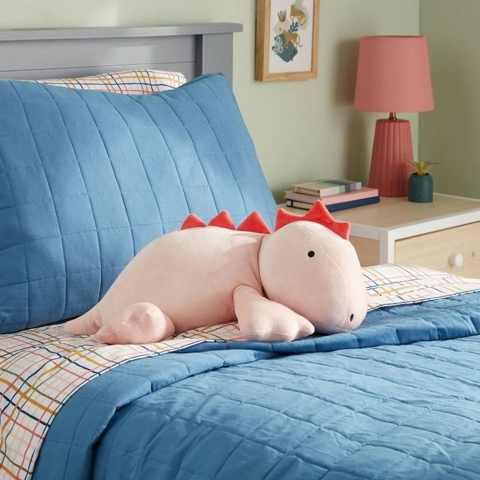 a pink dinosaur weighted pillow resting on a bed