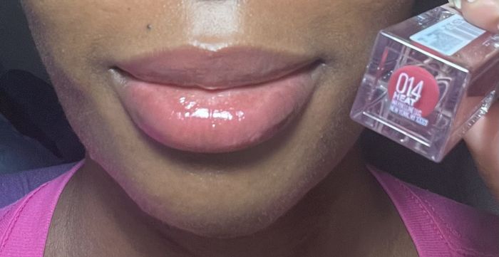 Reviewer wearing the Heat shade of lip gloss and holding the bottle