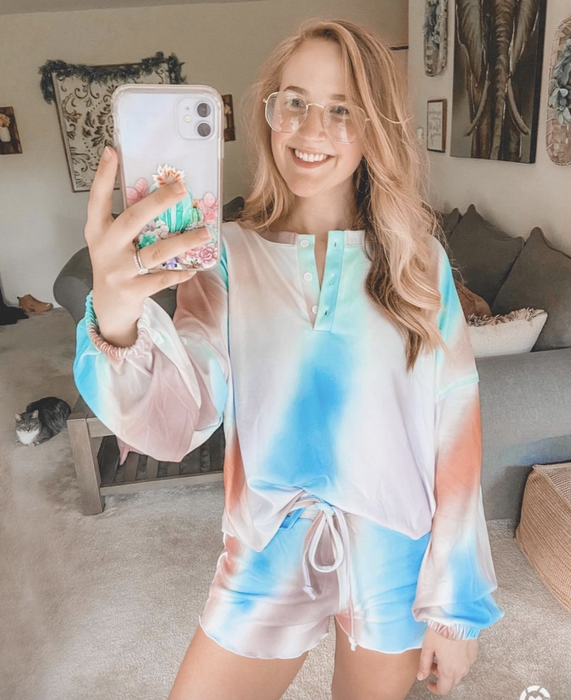A reviewer wearing drawstring shorts and a V-neck sleeved top in a tie-dye pattern with pink, blue, and orange