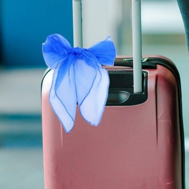 A blue scarf fastened to the handle of a pink suitcase, likely used for easy identification.