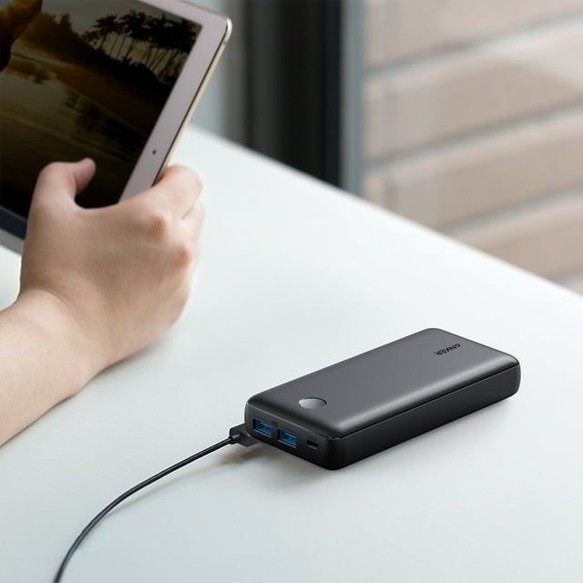 A person charges a tablet using a portable battery pack placed on a table.