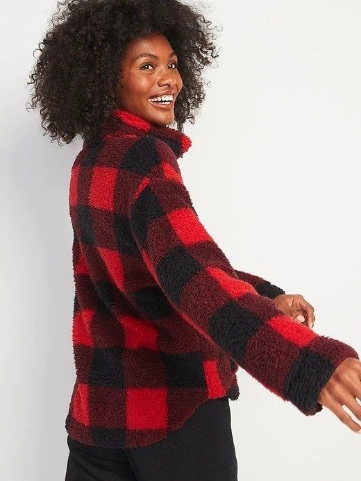 A woman happily glancing over her shoulder, wearing a stylish red and black plaid half-zip sweatshirt.