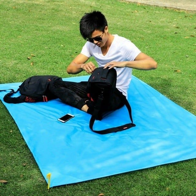 A person sitting on a blue mat outdoors, packing a black backpack.