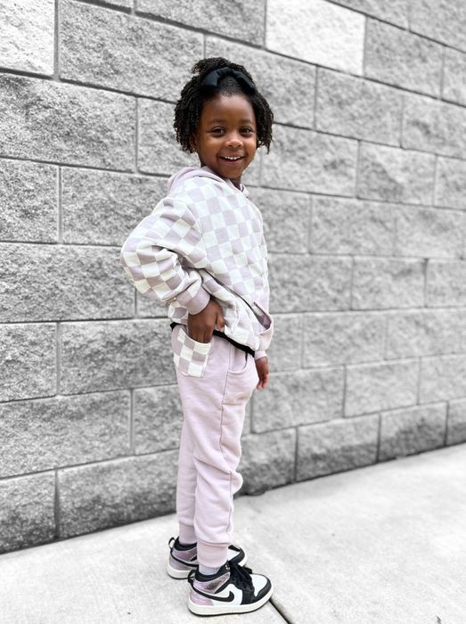 A child model wearing a lavender checkered hoodie and matching joggers