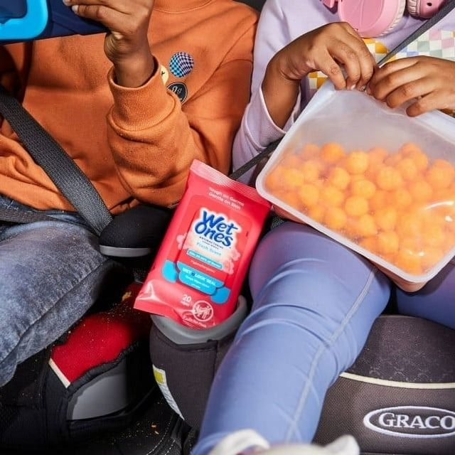 Two kids in car seats with a pack of Wet Ones and a container of cheese puffs.