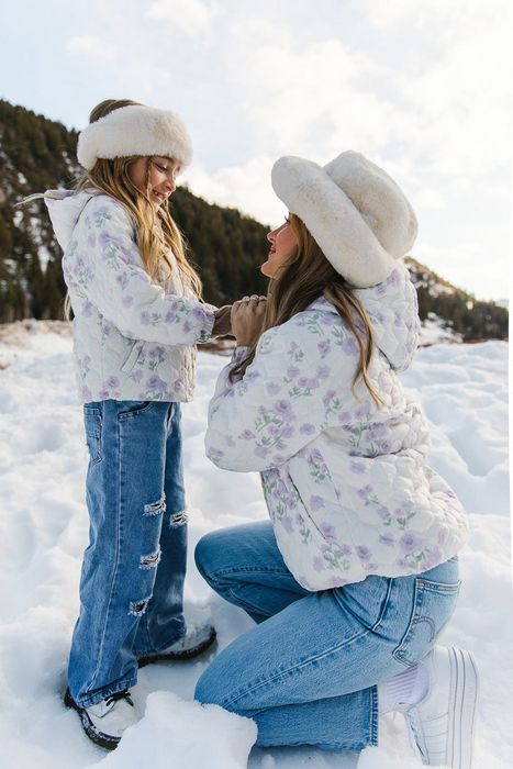 A child and adult wearing matching white quilted coats with lavender floral designs