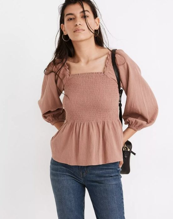 A model shows off a pink top, paired with blue jeans and carrying a chic black shoulder bag.