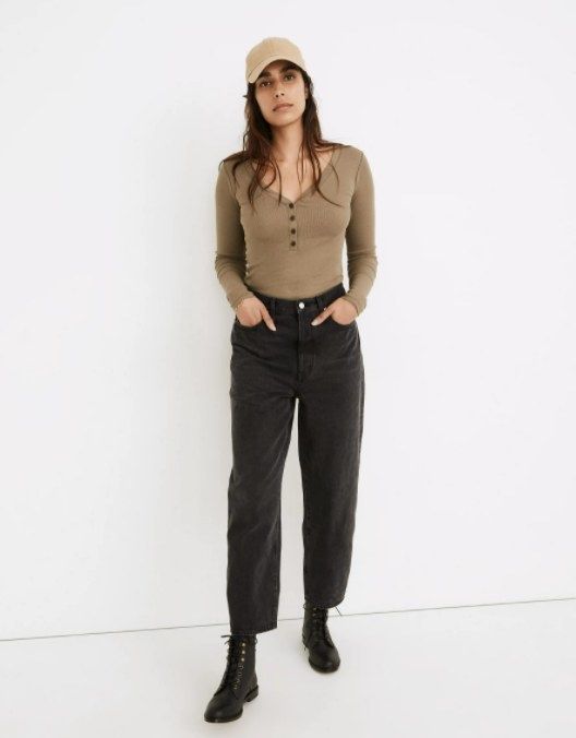 model wearing black balloon-leg jeans, paired with black lace-up boots, a brown long-sleeve shirt, and a tan baseball cap