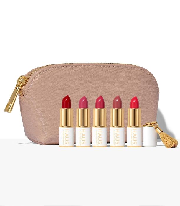 The five lipstick shades in red and pink tones are placed in front of a beige cosmetic bag.