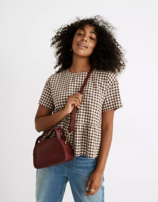model showcasing the burgundy crossbody paired with a brown and white gingham shirt and light blue jeans