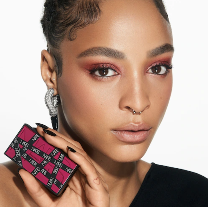 A model is holding the mini palette while wearing pink eyeshadow, showing off their look.