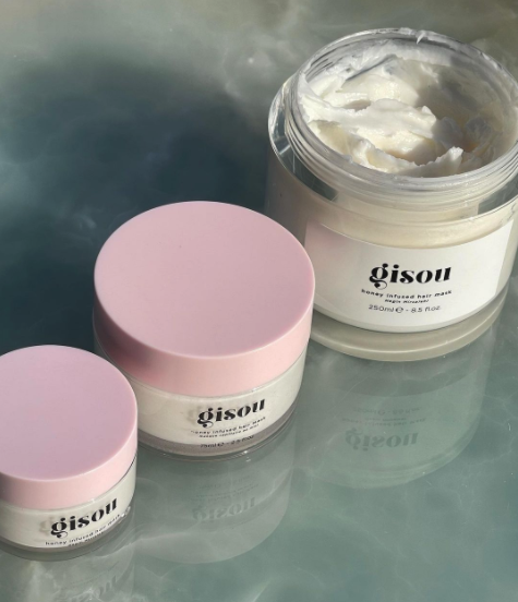 Three jars of the honey-infused hair mask with a pink lid. The smallest jar is on the left, and the full-size jar is on the right with the lid removed.