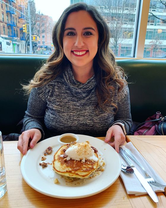 The author wearing lipstick while sitting at a table with a plate of pancakes