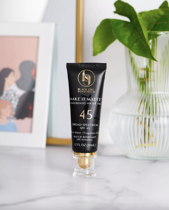 A tube of Black Girl Sunscreen rests on a counter, positioned in front of a plant and a picture frame.