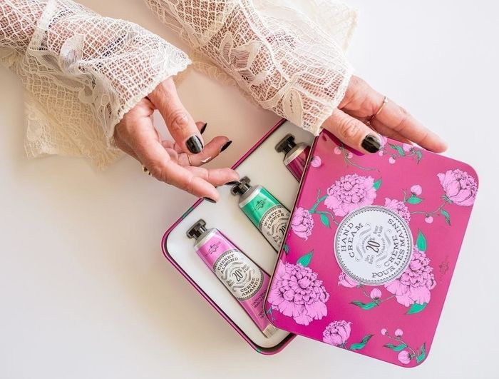 A model opens the pink tin, revealing three hand creams inside.