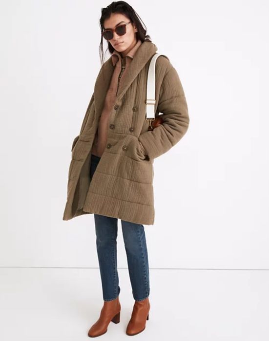 model styling the jacket with jeans, brown boots, a white handbag, and chic sunglasses