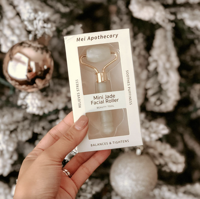 A model holding the packaged mini jade roller in front of a Christmas tree.