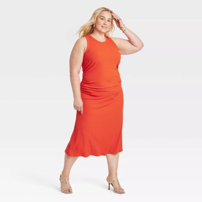 The model is wearing a sleeveless red fitted dress paired with open-toe sandals.