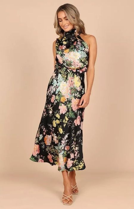 The model is wearing a sleeveless floral-patterned dress with a high neck and a mid-length hem.