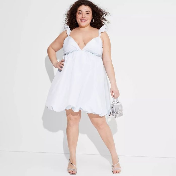 The model is wearing a white sundress featuring ruffle straps and a bubble hem.