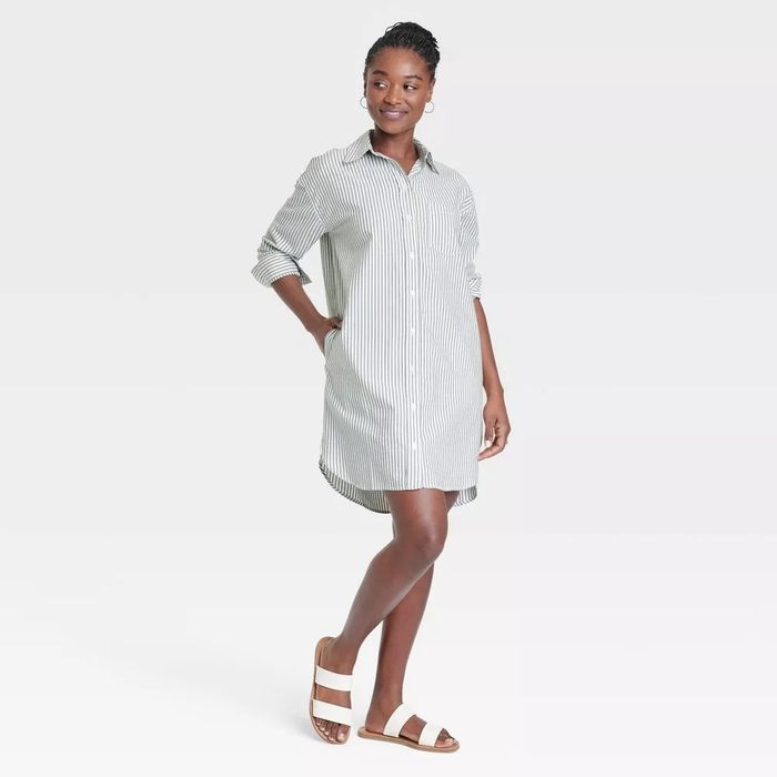 The model is wearing a striped button-down shirt dress paired with white sandals.