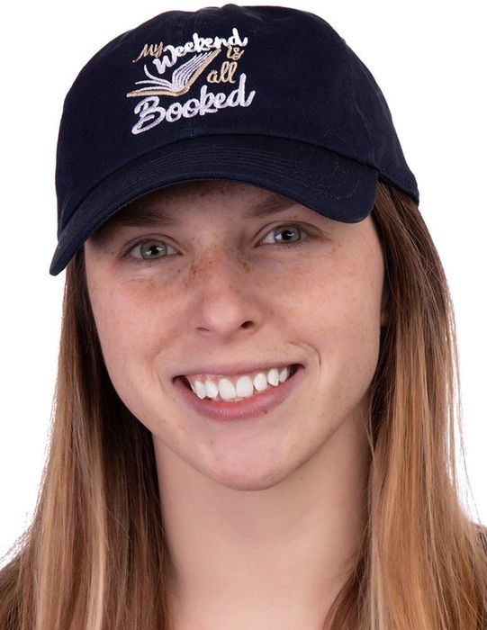 A navy cap featuring embroidered text that reads "my weekend is all booked" alongside a book design